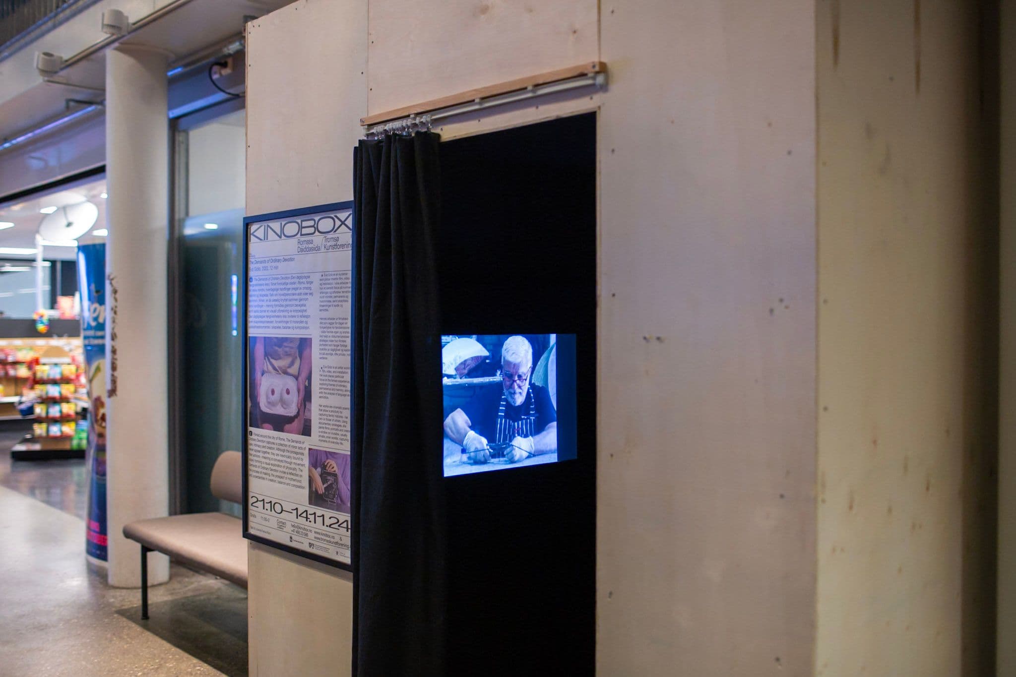 A film plays inside a wooden box. The interior is black. The box has a poster on the front and stands to the side of a kiosk