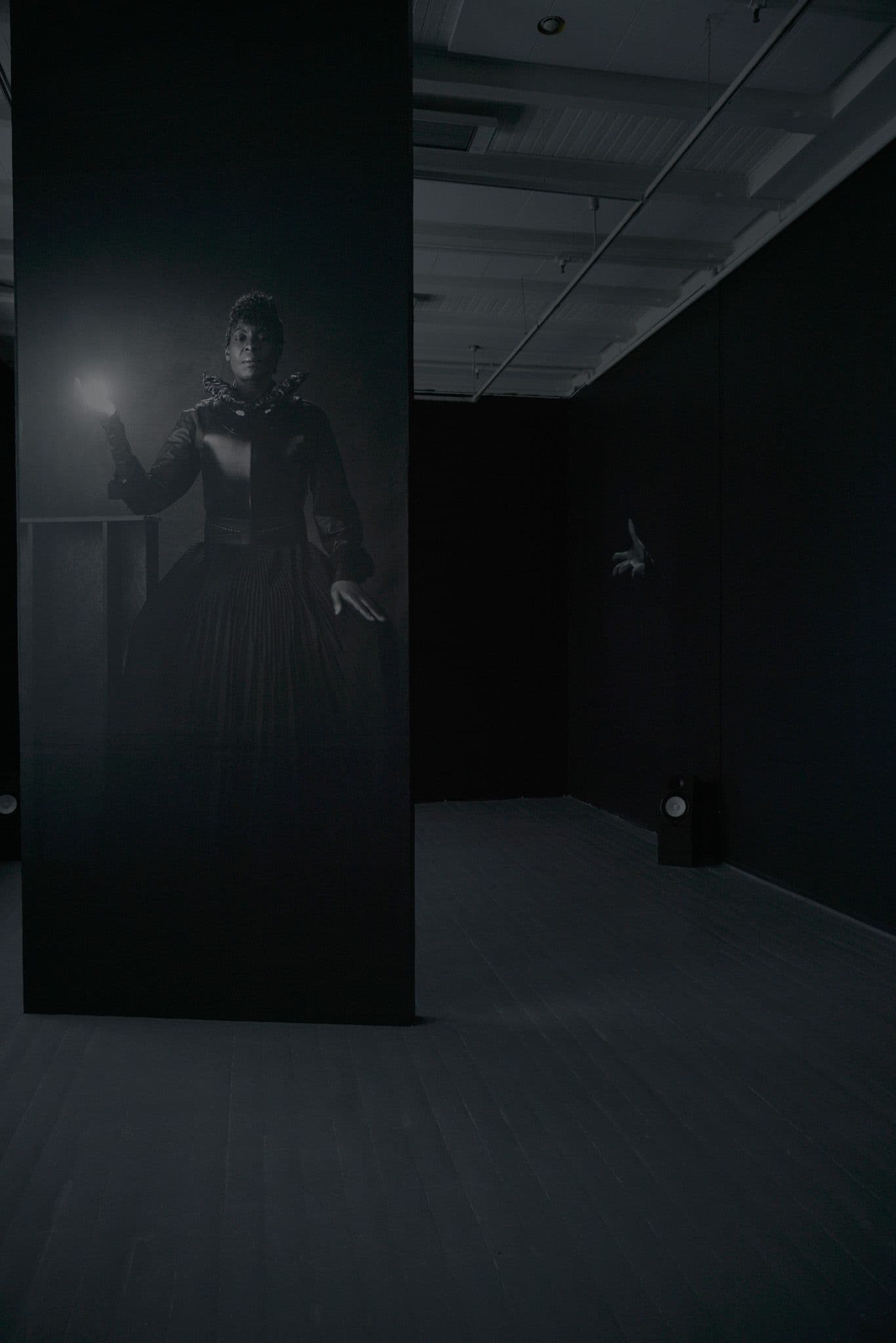 En dame i en svart kjole som holderen lyskule blir projisert på en svart vegg, i et svart rom.