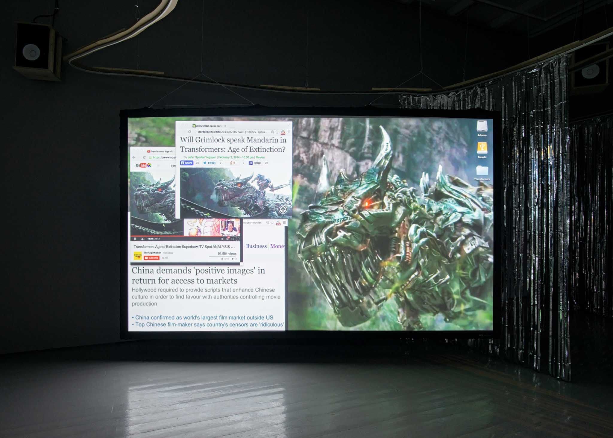 A bright projection screen in a gallery shows news clippings and a monster