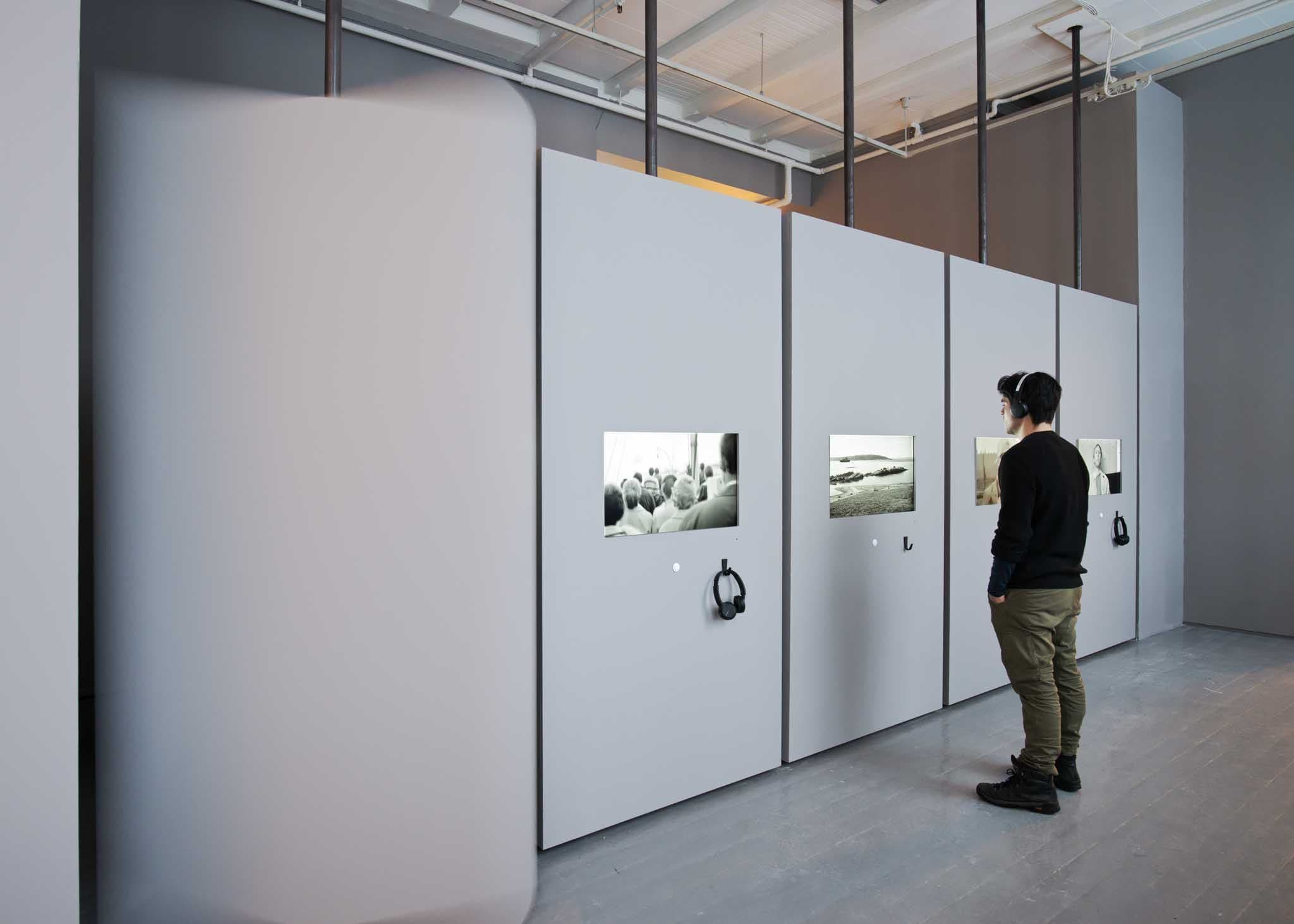 A man watches a black and white film in an installation, listening through headphones
