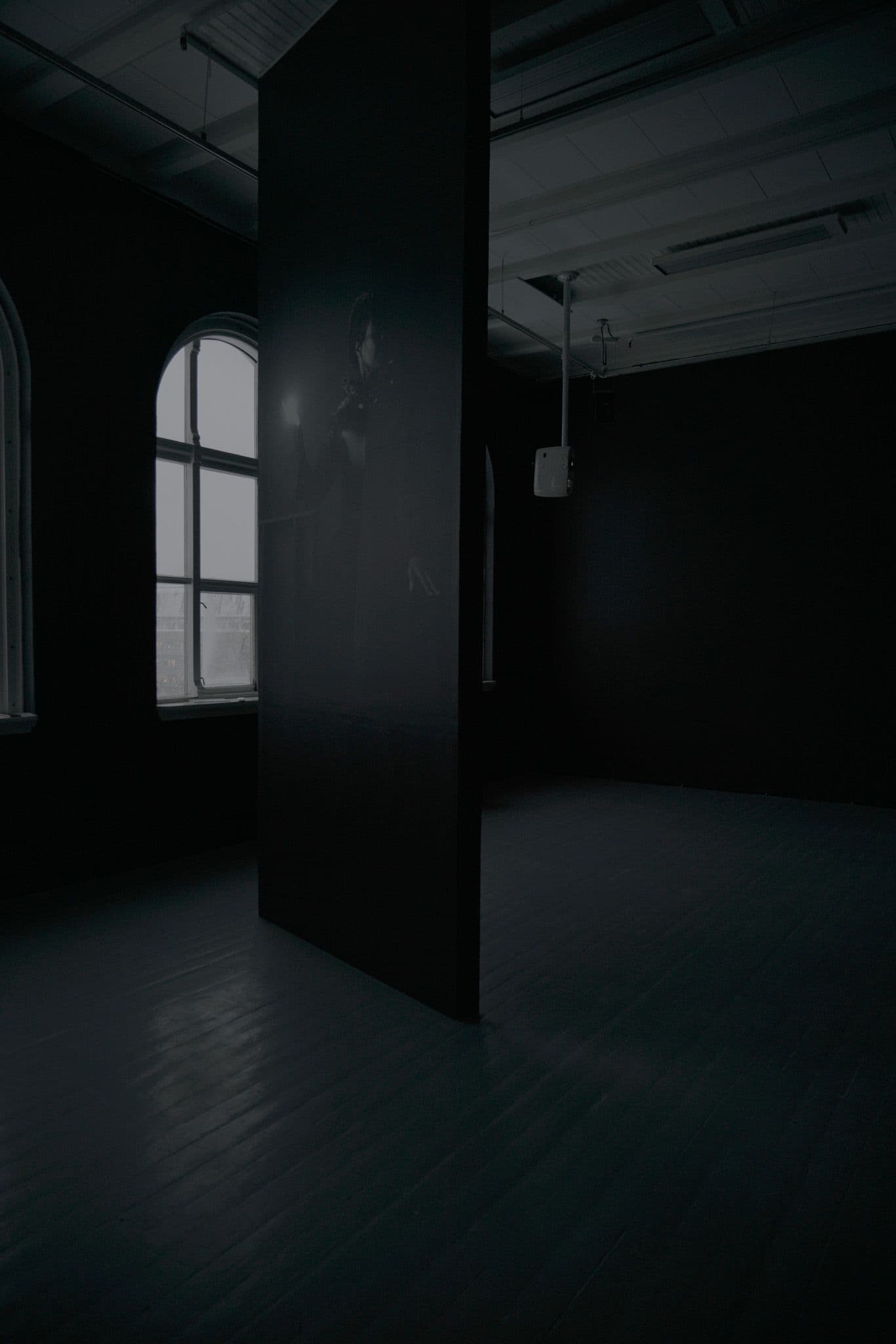 Et vertikalt panel fra gulv til tak viser en kvinne som holder en lyskule foran et vindu