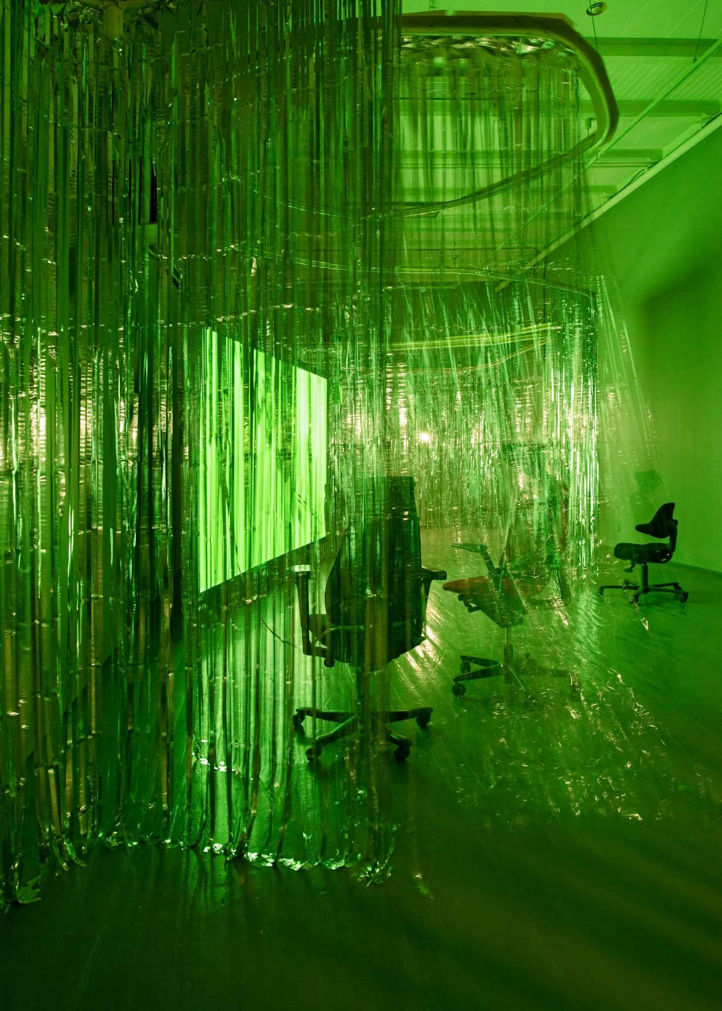 Kontorstoler er omgitt av foliegardiner i et gallerirom. Grønt lys fra et projeksjonslerret lyser opp rommet.