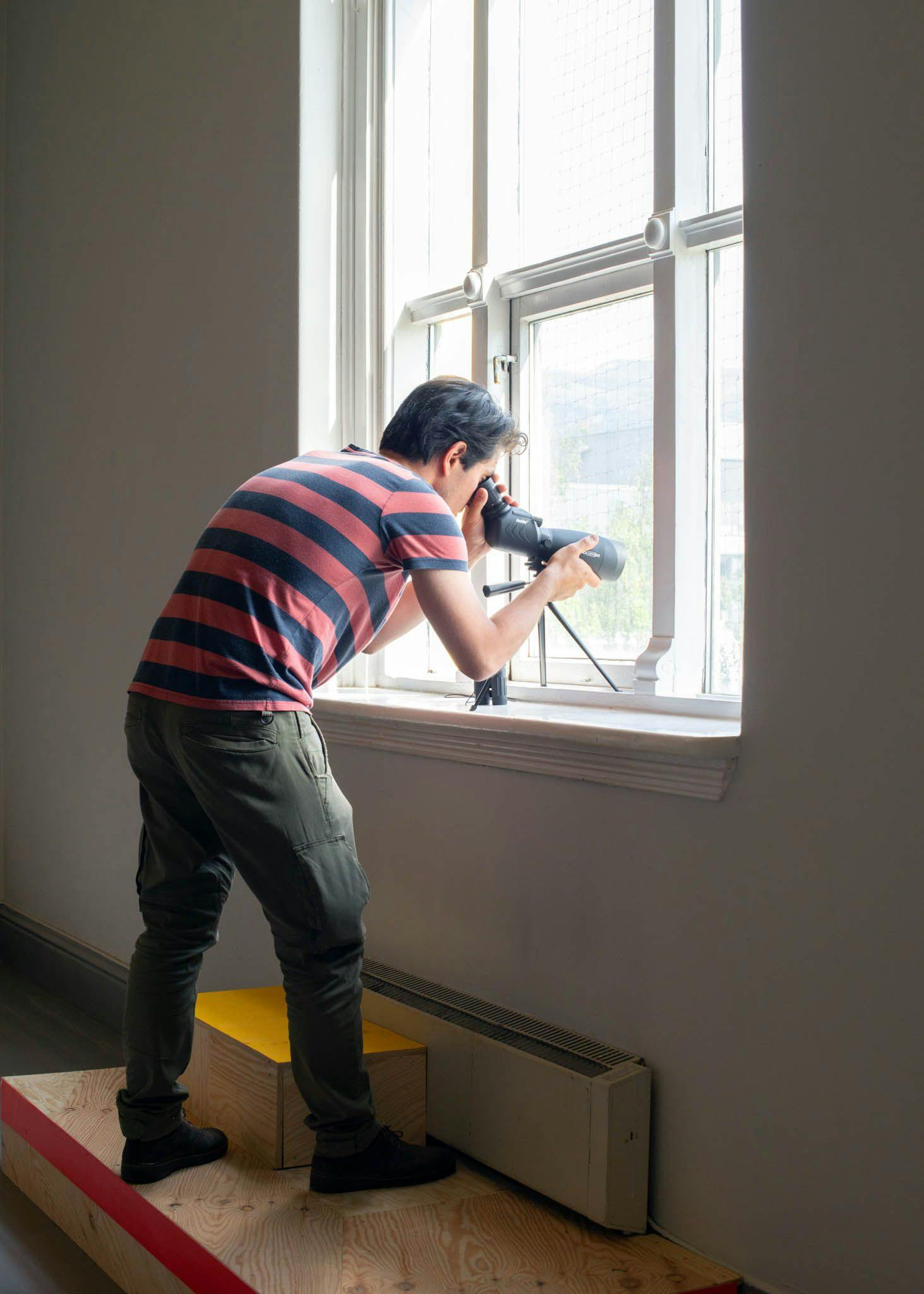 En mann ser gjennom et teleskop ut av et vindu